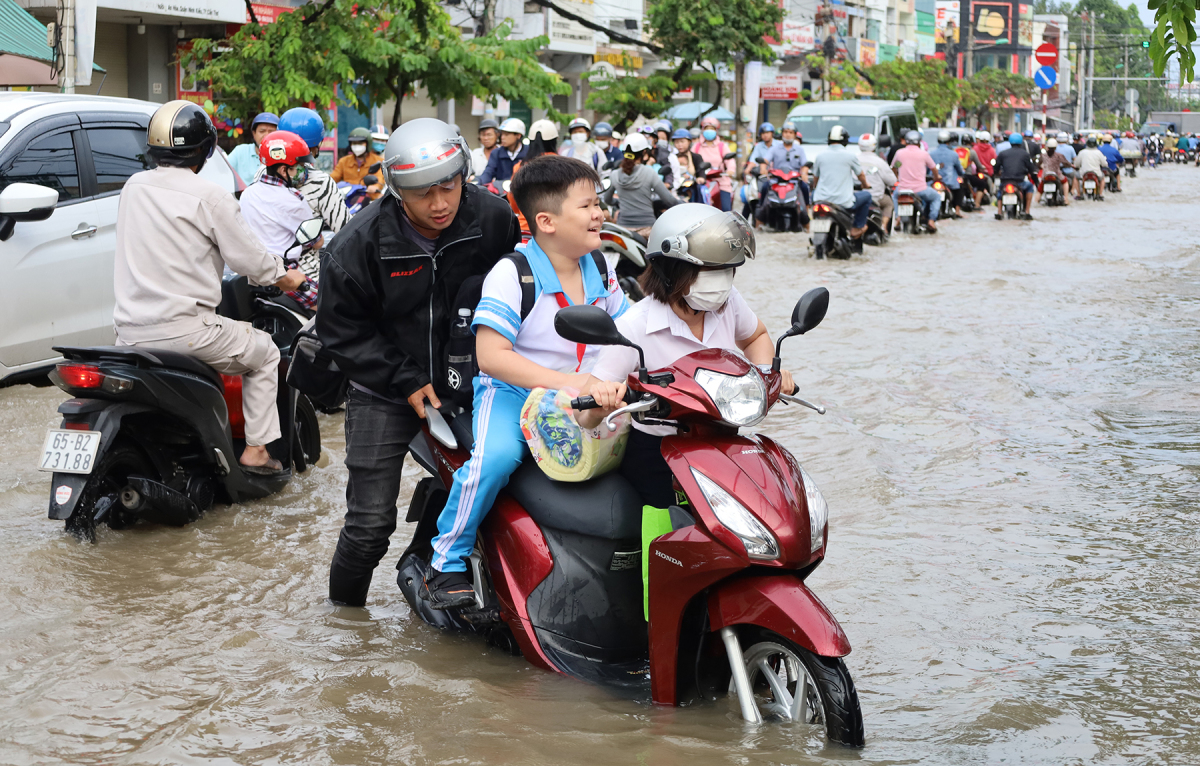 Trên đường Cách Mạng Tháng Tám (quận Ninh Kiều), xe của một phụ nữ đưa con đi học bị chết máy, được người đi đường hỗ trợ đẩy qua khu vực nguy hiểm. Ảnh: Vnexpress.
