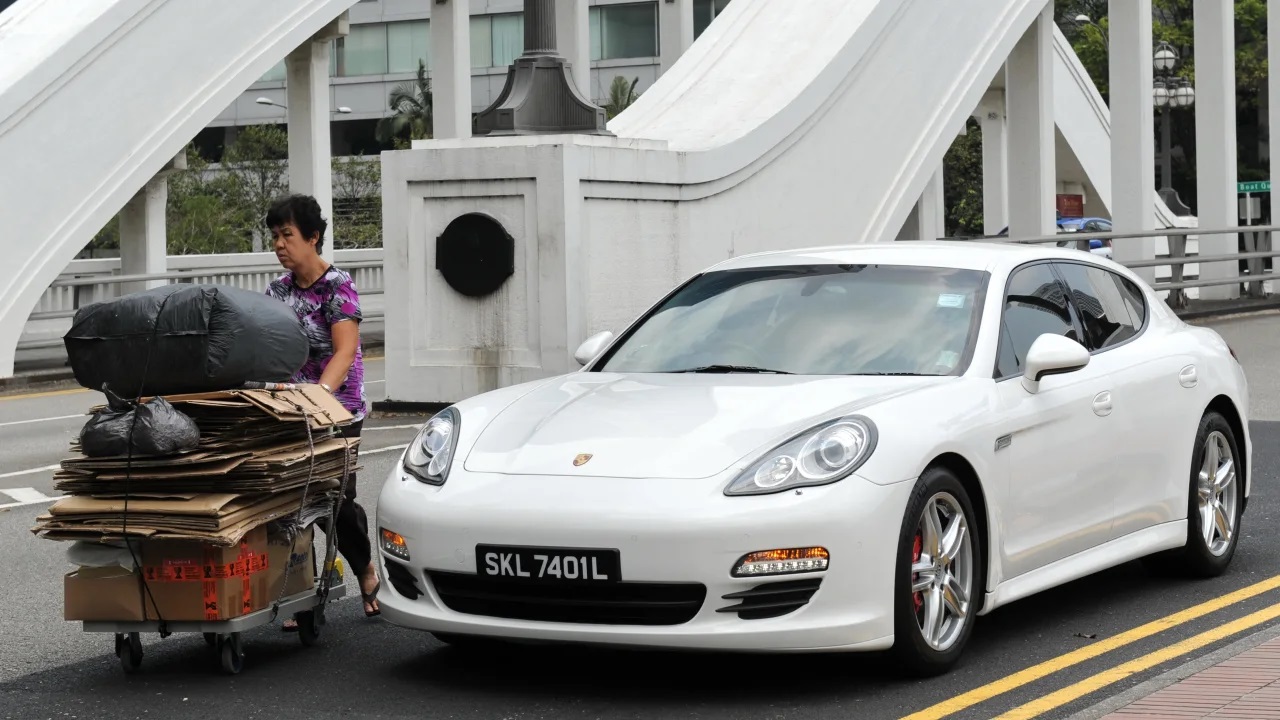 Một người phụ nữ đẩy xe chở rác tái chế qua một chiếc ô tô đắt tiền trên đường phố ở Singapore. Ảnh: AFP.