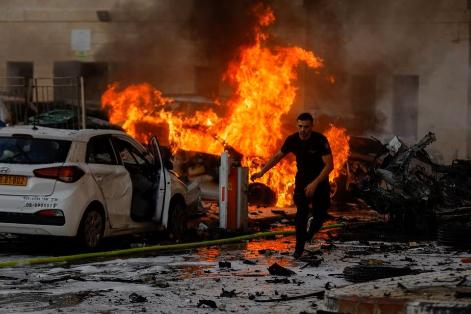 Một người đàn ông chạy trên đường khi tên lửa từ Gaza khiến nhiều ô tô ở Ashkelon, Israel, phát nổ. Ảnh: Reuters.