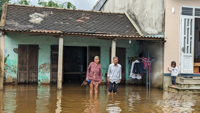 Vợ chồng ông Nguyễn Dẫn và bà Hồ Thị Bé (78 tuổi) trước sân nhà trưa 16/10. Thời điểm chúng tôi có mặt, nước lụt vẫn ngập cao đến đồi gối dù trợi đã tạnh mưa được 2 ngày và các xóm xung quanh nước đã rút hết. 