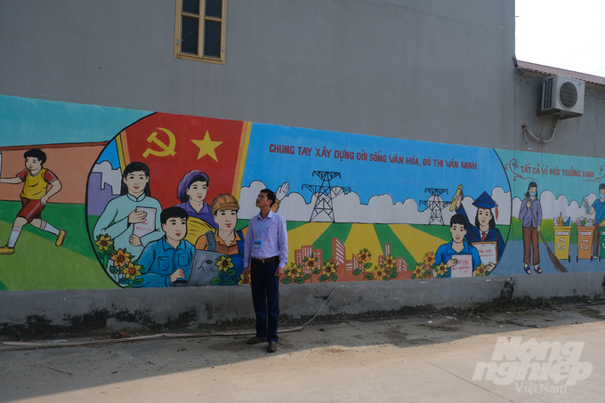 Anh Nguyễn Viết Trang, Phó Chủ tịch UBND xã Trung Sơn (huyện Việt Yên), bên bức tranh tường dài cả chục mét vừa hoàn thiện ở thôn Quả. Ảnh: K.Trung.