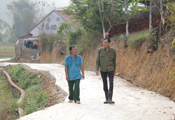 Ông Triệu Văn Thắng (bên phải) đi trên con đường bê tông mới làm xong qua thôn. Ảnh: Ngọc Tú. 