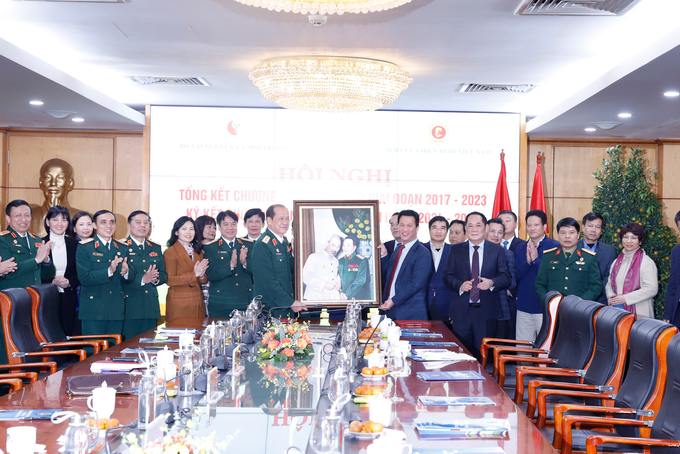 Bộ trưởng Đặng Quốc Khánh cùng Thượng tướng Bế Xuân Trường và các đại biểu chụp ảnh lưu niệm bên bức tranh Chủ tịch Hồ Chí Minh và Đại tướng Võ Nguyên Giáp.