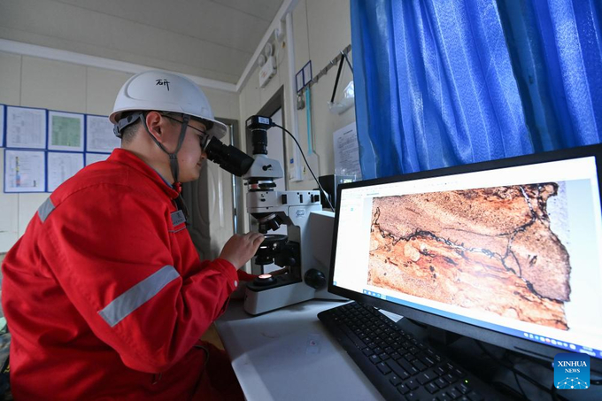 Một nhà nghiên cứu đang nghiên cứu mẫu đất được thu thập từ lòng đất sâu qua kính hiển vi tại hố khoan Shenditake 1. 