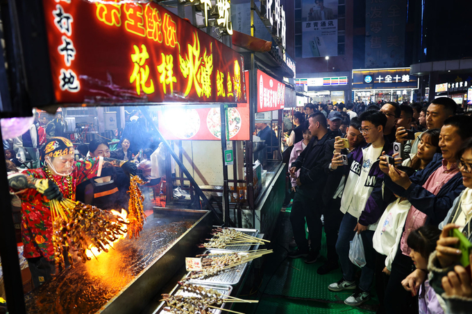 Du khách quay video cảnh người bán hàng nướng thịt xiên trên ngọn lửa lớn tại Chợ đêm Chính Định ở tỉnh Hà Bắc. Ảnh: CGTN.