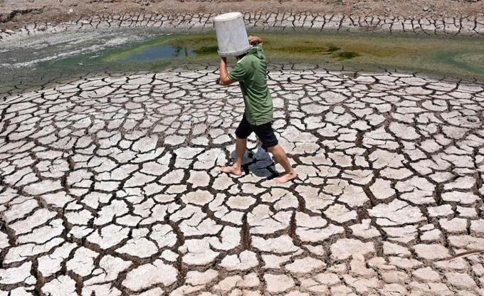 A man carries a plastic bucket across the cracked bed of a dried-up pond in Vietnam’s southern Ben Tre province on March 19. Photo: AFP