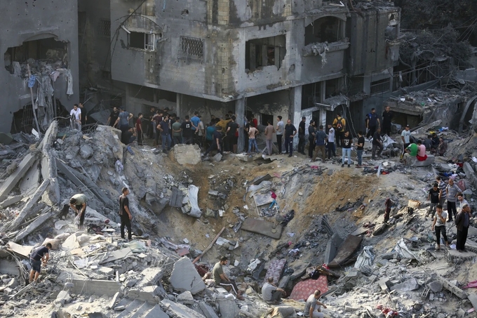 Người Palestine đứng quanh một hố bom từ cuộc không kích của Israel hồi tháng 11/2023. Ảnh: AFP.