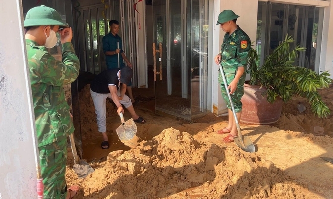 Lực lượng chức năng hỗ trợ người dân khắc phục bùn đỏ tràn vào nhà. Ảnh: KS.