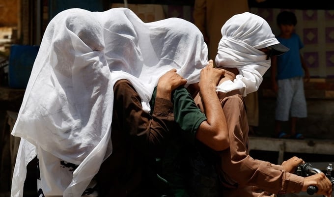Người dân Pakistan chùm khăn ướt để làm mát khi đi xe máy giữa nắng nóng 52 độ C ở Jacobabad, Pakistan, hôm 26/5. Ảnh: Reuters.