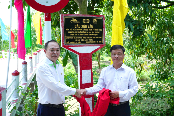 Ông Nguyễn Ngọc Tâm, Phó Tổng Giám đốc Công ty Cổ phần Nhựa Thiếu niên Tiền Phong phía Nam (ảnh trái) và ông Nguyễn Minh Cảnh, Phó Bí thư Thường trực, Chủ tịch HĐND xã Mỹ Xương thực hiện nghi lễ tháo khăn phủ biển tên cầu Xẻo Ván - Cầu nối yêu thương số 108. Ảnh: Lê Hoàng Vũ.