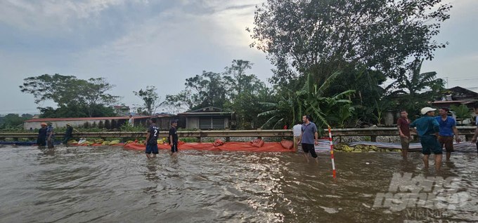 Người dân dùng bao tải và bạt để ngăn nước từ Quốc lộ chảy vào khu dân cư. Ảnh: Quốc Toản.