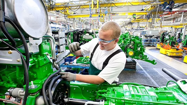 John Deere staff work on farming equipment. The company is laying off workers.