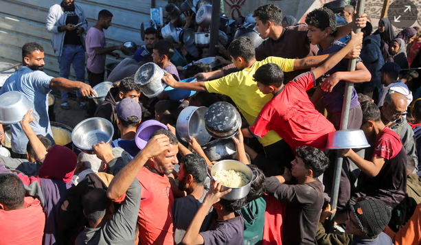 People scramble to receive food cooked by a charity kitchen in Khan Younis. Photograph: Hatem Khaled/Reuters.