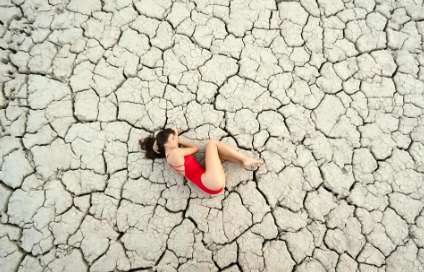 A woman lying on cracked arid earth. There is no food on a drought-stricken planet.