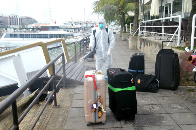Nhân viên y tế Quảng Ninh tiến hành khử trùng hành lý khách du lịch bị đưa đi cách ly tại cảng tàu Quốc tế Tuần Châu, Hạ Long vào trưa nay. Ảnh: BQN