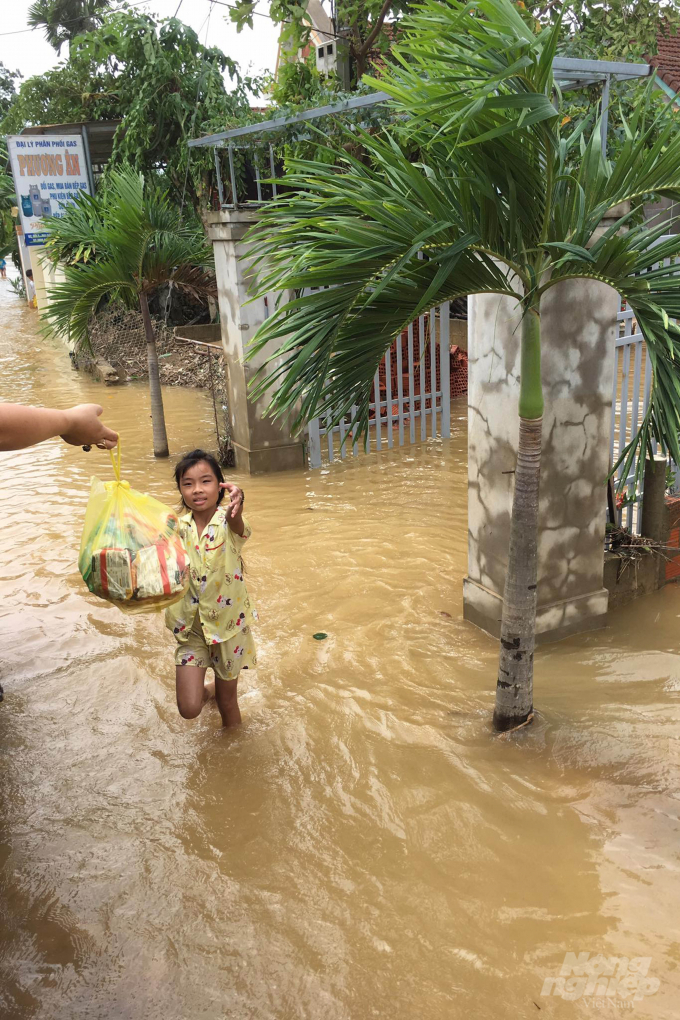 Nước vẫn chưa rút hết nhưng khi nghe có đoàn thiện nguyện vào xã, một bé gái đã đứng đợi sẵn trước cổng nhà để nhận quà. Ảnh: Hải Yến.