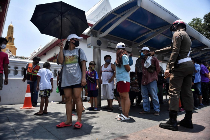 Cảnh sát hướng dẫn người lao động thất nghiệp thực hiện giãn cách xã hội khi đi nhận đồ phát chẩn tại thủ đô Bangkok. Ảnh: AFP
