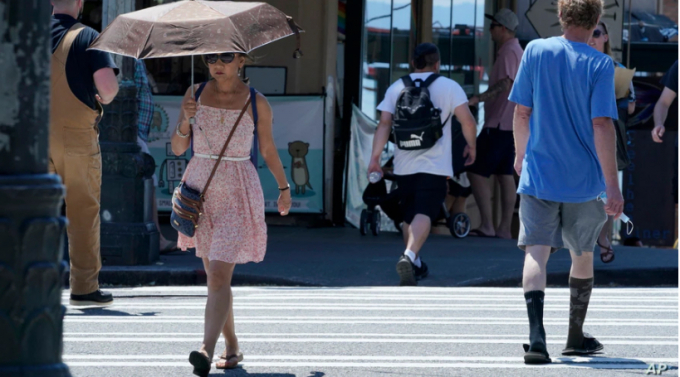 A women uses an umbrellra for shade from the sun while walking near Pike Place Market, June 29,2021, in Seattle.   