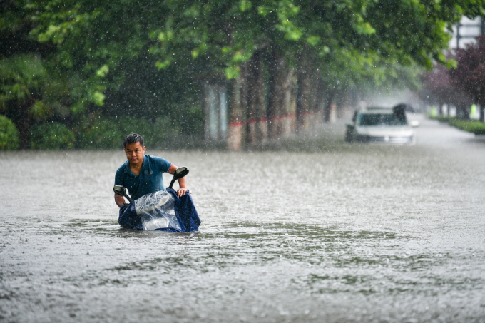 Một người dân ở thành phố Trịnh Châu vật lộn với chiếc xe máy trong trận mưa chiều 20/7. Ảnh: CND 