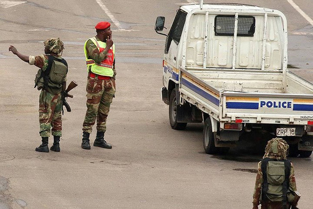   Một quân nhân Zimbabwe (mũ đỏ) dường như mặc thêm 1 lớp áo của cảnh sát, đứng bên 1 chiếc xe cảnh sát ở giao lộ. Ảnh: Reuters.  