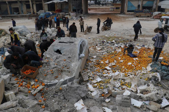 Người dân thu lượm số cam bị rơi vãi sau một cuộc không kích nhằm vào khu chợ do phiến quân kiểm soát ở thành phố Maarrat Misrin, tỉnh Idlib, Syria ngày 14/1.
