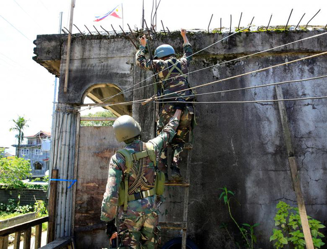 Theo người phát ngôn của Tổng thống Philippines, ông Ernesto Abella, các phần tử khủng bố vẫn đang tiếp tục sử dụng dân thường làm lá chắn sống và nhốt họ trong các nhà thờ Hồi giáo để đối đấu với quân đội chính phủ. Trong ảnh: Các binh sĩ Philippines trèo lên mái nhà để truy tìm dấu vết của các phiến quân khủng bố ở Marawi.