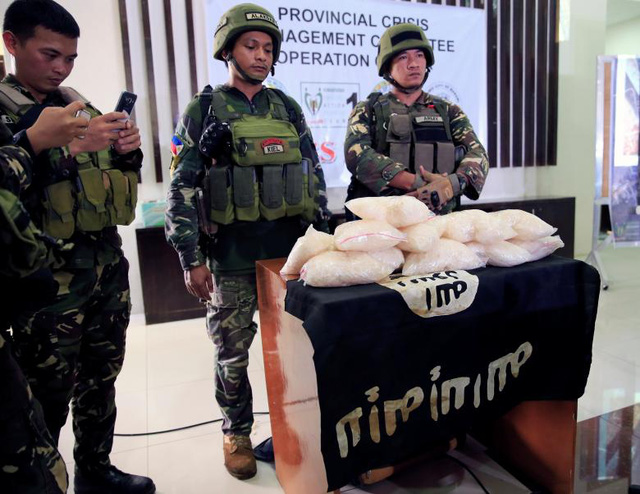 Quân đội Philippines cho biết hiện còn khoảng 100 phiến quân đang cố thủ tại Marawi. Trong ảnh: Các binh sĩ Philippines công bố tang vật gồm 11 kg ma túy đá, ước tính từ 2,2-5 triệu USD, và cờ của IS thu được từ các tay súng của nhóm phiến quân Maute.