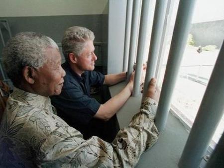 South African President Nelson Mandela, foreground, and U.S. President Bill Clinton peer out from Section B, prison cell No. 5, on Robben Island, South Africa March 27, 1998. Mandela spent 18 years of his 27-year prison term on the island.