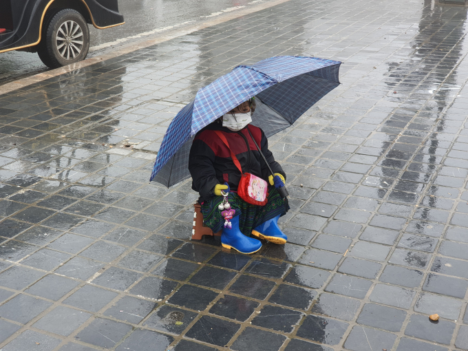 Trong ảnh là một em bé cầm ô ngồi giữa mưa rét để bán nốt những sản phẩm lưu niệm cuối cùng. Có vẻ như vị trí ngồi, tiện đường qua lại ngay giữa trung tâm thị xã Sa Pa cũng được bố mẹ em bé chọn khá kỹ càng. 