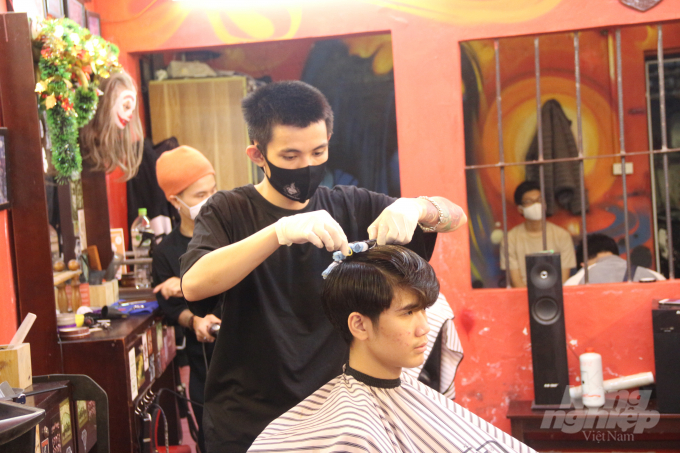 Anh Trịnh Hiếu (áo đen), một thợ cắt tóc tại cửa hàng, trao đổi với NNVN: 'Mới có 6 - 7 tiếng từ khi mở hàng mà tôi đã cắt cho hơn 10 khách trong khi ngày trước có những hôm cả ngày chỉ có 5 - 6 khách.' Ảnh: Phạm Hiếu.