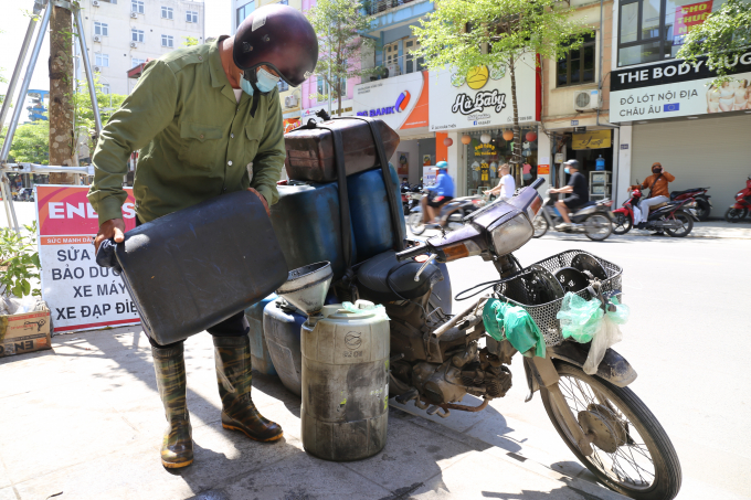 Một người thu gom dầu thải nhẫn nại dưới cái nóng như thiêu đốt đi khắp các cửa hàng sửa chữa xe máy để gom dầu.