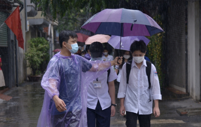 Thanh niên tình nguyện che mưa cho thí sinh trong sáng 13-6 tại một điểm thi quận Thanh Xuân.