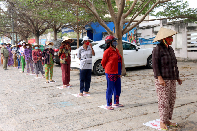 Người dân nhận gạo xếp hàng theo vị trí đã kẻ sẵn, đảm bảo khoảng cách giãn cách an toàn theo quy định phòng, chống dịch. Ảnh: NT.