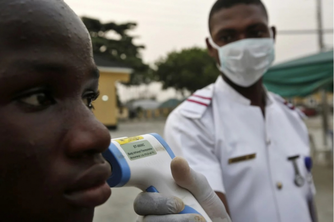 Quan chức y tế của quân đội Nigeria thực hiện đo nhiệt độ cho một người đến bệnh viện ở Lagos. Ảnh: Bloomberg.
