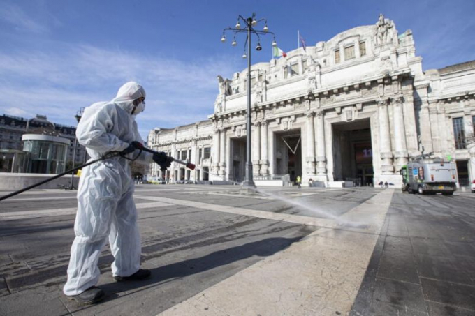 Người của Công ty Dịch vụ Môi trường Milan mặc quần áo bảo hộ, đeo khẩu trang và kính bảo vệ phun xịt khử trùng quảng trường của Nhà ga Trung tâm hôm 13/3. Ảnh: ANSA/EPA-EFE.