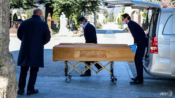 Những người phục vụ đeo khẩu trang đỡ một cỗ quan tài ra khỏi một chiếc xe tang tại nghĩa trang Monumental của Bergamo, Lombardy (Italia). Ảnh: Piero Cruciatti/AFP.