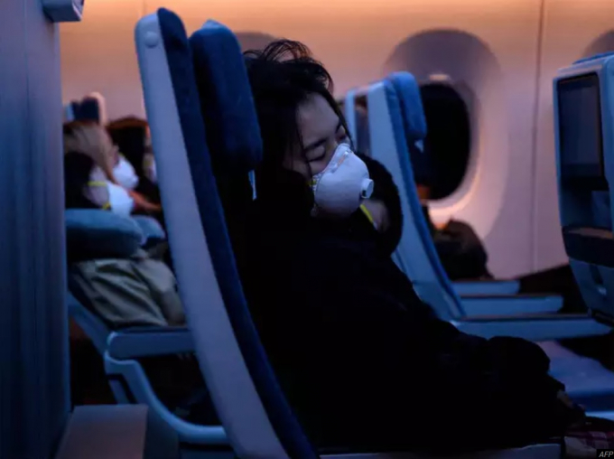 Một hành khách đeo khẩu trang ngủ trên máy bay. Ảnh: AFP.