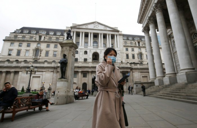 Một phụ nữ đeo khẩu trang đi bộ trước Ngân hàng Anh, ở London, sau khi đại dịch Covid-19 bùng phát. Ảnh: Reuters.