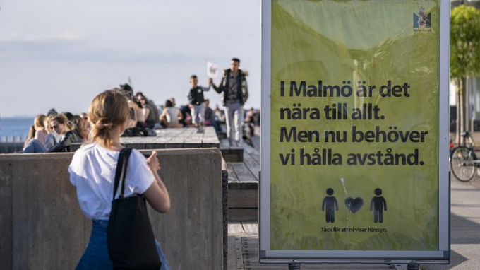 Người dân ra ngoài tận hưởng thời tiết ấm áp ở Malmo, Thụy Điển, hôm 26/5/2020. Cạnh đó là một tấm biển có nội dung: 'Ở Malmo mọi thứ đều gần gũi. Nhưng bây giờ chúng ta cần giữ khoảng cách'. Ảnh: AP.