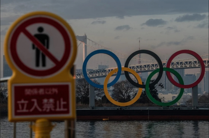 Một biển cảnh báo gần biểu tượng Olympic ở Tokyo, Nhật Bản. Sẽ có các quy trình nhập cảnh nghiêm ngặt, tương tự như quy định đối với một số ít du khách hiện tại đến Nhật Bản, được áp dụng cho các vận động viên tới tham dự Olympic.