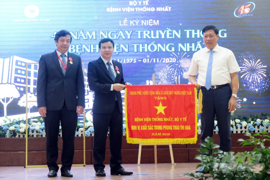 Thứ trưởng Bộ Y tế Đỗ Xuân Tuyên (áo trắng) trao tặng cờ 'Đơn vị xuất sắc trong phong trào thi đua' của Chính phủ cho Bệnh viện Thống Nhất. Ảnh: Đ.H.