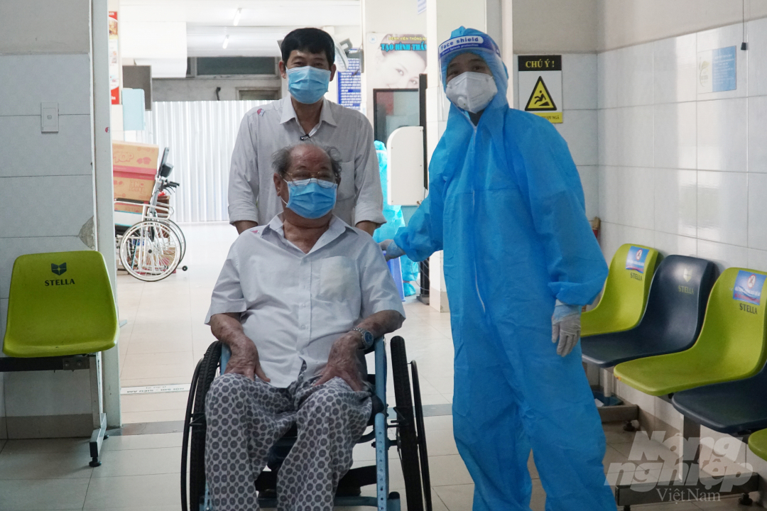 Nhân viên y tế hướng dẫn người nhà đưa ông Hồ Kỳ Thơ đến khu vực khám sàng lọc. Ảnh: Nguyễn Thủy.
