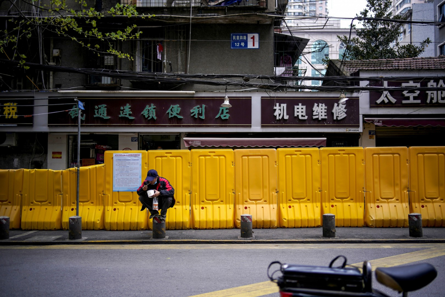Người đàn ông ngồi ăn mỳ trong bữa sáng cạnh hệ thống hàng rào ngăn Covid-19 trên đường phố Vũ Hán.