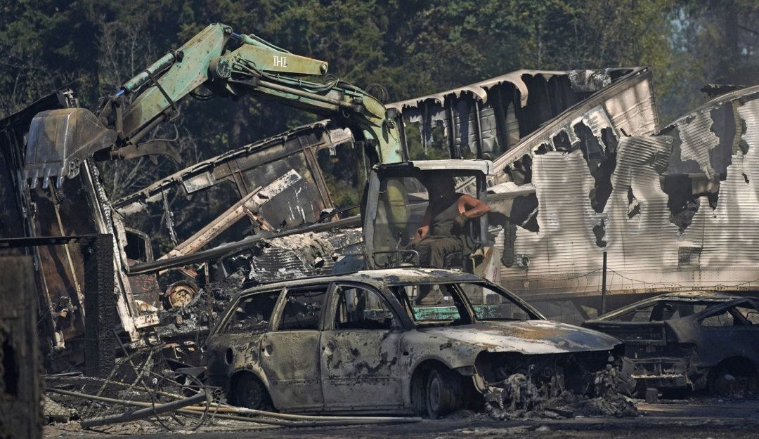 Người đàn ông lái máy xúc dọn dẹp những phương tiện bị lửa cháy rừng thiêu trụi trong đêm ở Graham, Washington.