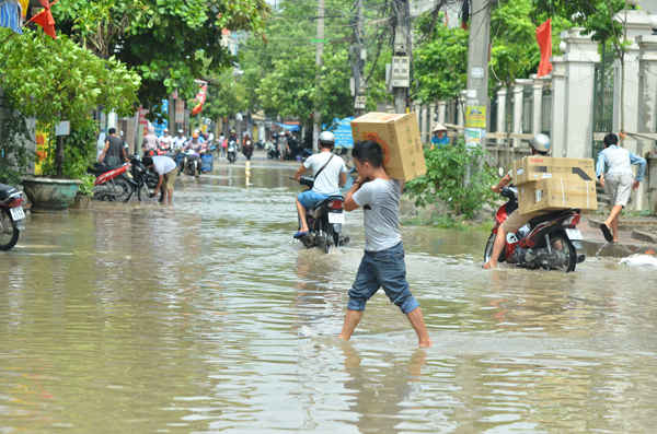 Nước ngập xe không di chuyển vào được, chàng thanh niên phải vác từng chiếc thùng hàng vào cửa hàng
