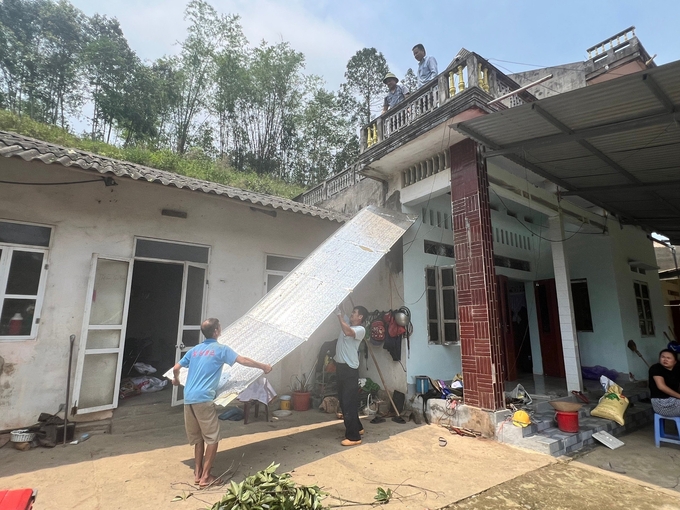 z5359619945509_991d7ef8306cf66cfb206e93e3108f6e-172241_937.jpg Gia đình ông Trần Văn Bốn cùng hàng xóm đang lợp lại mái nhà. Ảnh: Ngọc Tú.
