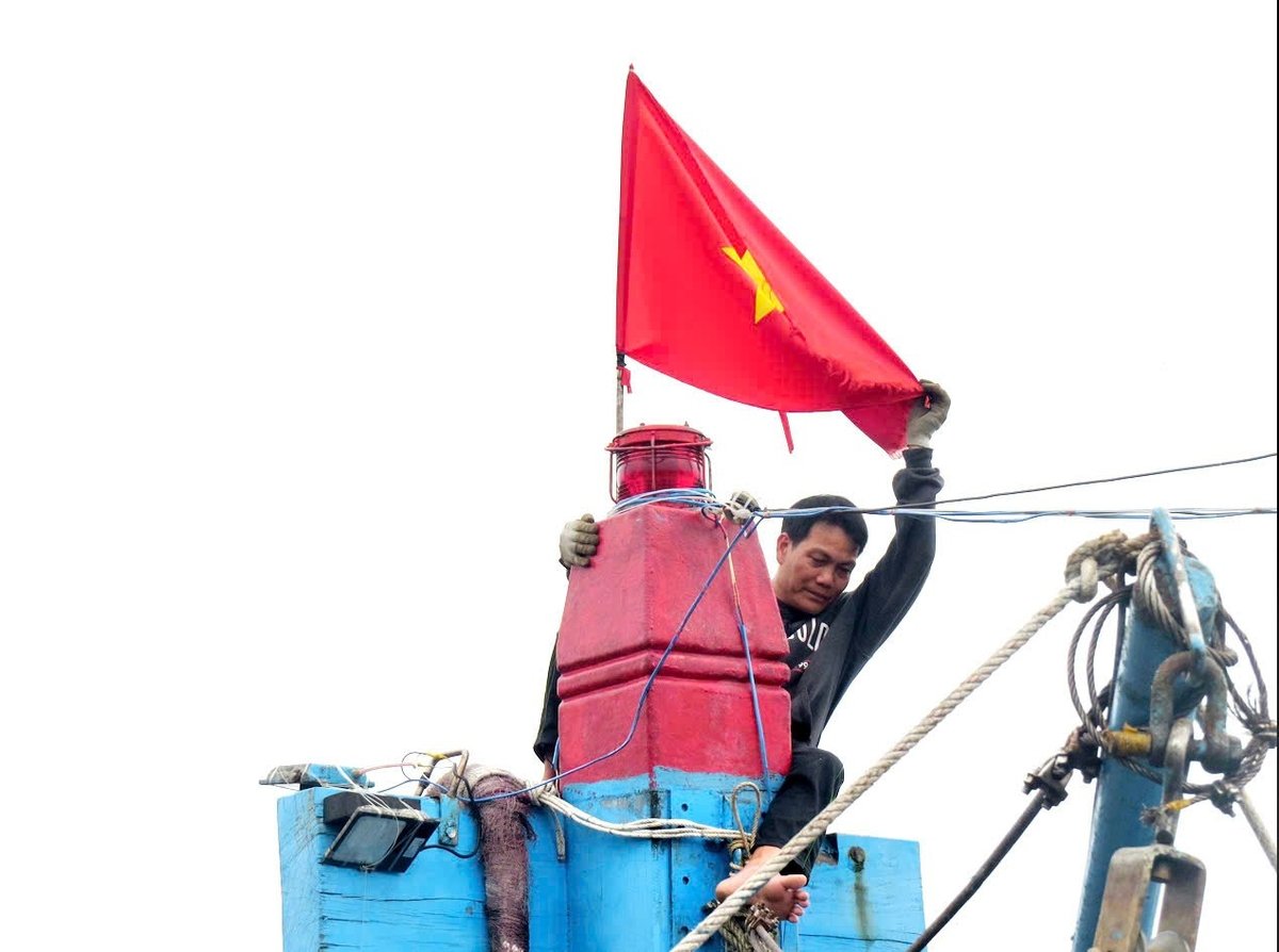 Ngư dân Ngô Tấn Lộc chỉnh sửa thiết bị gắn trên cột tàu trước chuyến ra khơi. Trên đỉnh cột tàu là lá cờ Tổ quốc - điều không thể thiếu của mỗi con tàu trong những chuyến vươn khơi. Ảnh: Võ Thanh Kỳ.