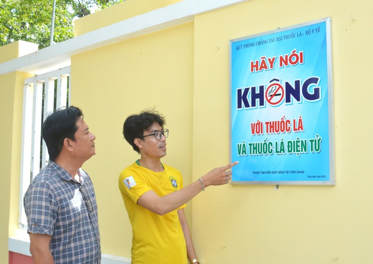 Thầy Nguyễn Thành Thông (bìa trái), Phó Hiệu trưởng Trường THCS và THPT Võ Văn Kiệt và Bí thư Đoàn trường Lý Hoàng Luân bên tấm biển tuyên truyền về phòng, chống tác hại của thuốc lá được gắn ở khuôn viên trường để học sinh dễ tiếp cận. Ảnh: Trung Chánh. Thầy Nguyễn Thành Thông (bìa trái), Phó Hiệu trưởng Trường THCS và THPT Võ Văn Kiệt và Bí thư Đoàn trường Lý Hoàng Luân bên tấm biển tuyên truyền về phòng, chống tác hại của thuốc lá được gắn ở khuôn viên trường để học sinh dễ tiếp cận. Ảnh: Trung Chánh.