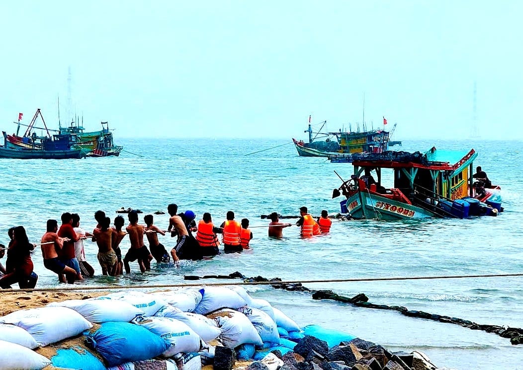 Lực lượng biên phòng phối hợp cùng người dân kéo tàu cá gặp nạn vào bãi biển để trục vớt, giảm thiểu thiệt hại. Ảnh: CTV.