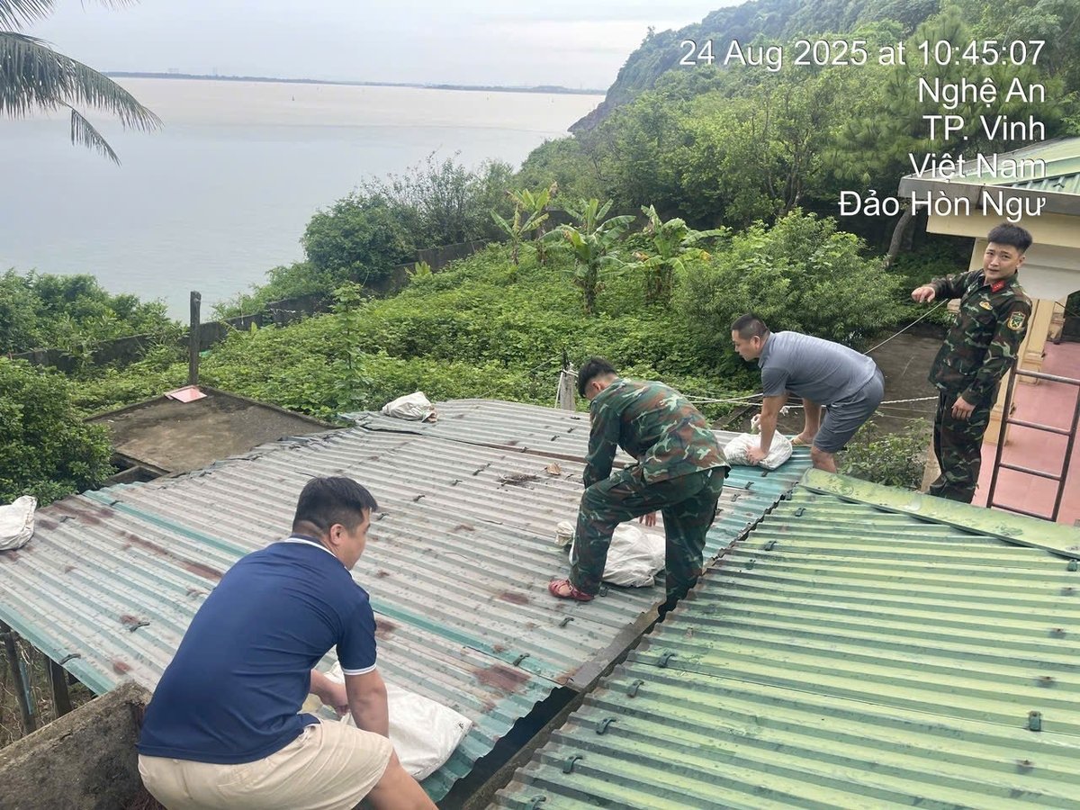 Cán bộ Trạm Khí tượng Hải văn Hòn Ngư (tỉnh Nghệ An) cùng bộ đội đảo Hòn Ngư đặt vật nặng tránh tốc mái nhà trạm. Ảnh: Trà My. 